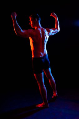 Stüdyoda poz veren kaslı bir adam resmi, koyu beyaz arka plan.