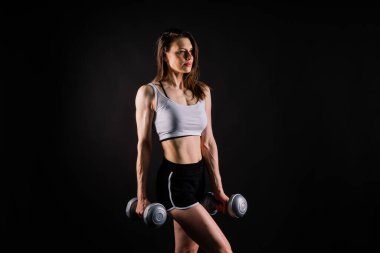 Sportif kadın, dambıllarla egzersiz yapıyor. Silüet stüdyosu koyu sarı arka plan.