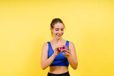 Stüdyonun arka planında çörek yiyen genç, tatlı spor kadın.