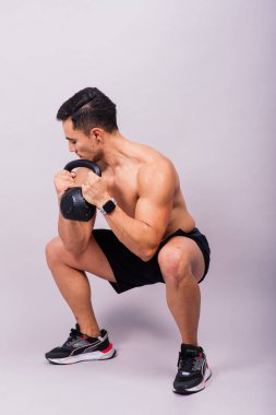 Güçlü, genç, kaslı, formda ve kaslı bir adam elinde ağır kettlebell tutuyor.