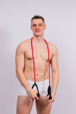 Beyaz külotlu kaslı vücut sporcusu lastik ile fiziksel egzersiz yapıyor.