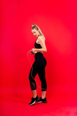 Stüdyoda ip atlayan sarışın kadın, sarı kırmızı ve koyu arkaplan.