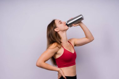 Beyaz arka planda izole edilmiş su içen kaslı bir kadın.