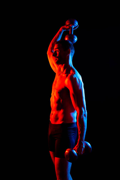 Взрослый мускулистый мужчина улыбается и кричит во время тренировки с гантелями.