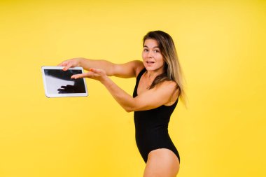 Stüdyoda sarı arka planda, tablet dizüstü bilgisayarı olan bir kadın.