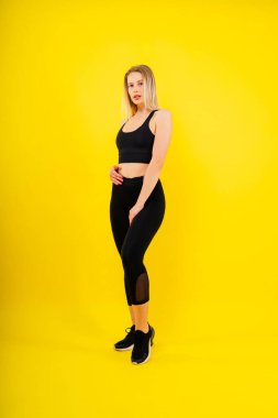 Stüdyoda sarı siyah arka planda izole edilmiş genç bir kadının portresi, fitness veya vücudu..