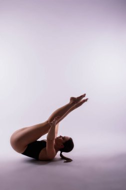 Siyah elbiseli genç bir bayan yerde yoga pozları veriyor.