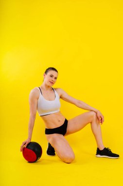 Spor Kafkas haçı kadın fitness topu ile uyumlu, kameraya bakın. Stüdyo koyu sarı arkaplan