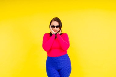 Genç, gülümseyen, kilolu, spor giyimli bir kadının tam boy fotoğrafı.