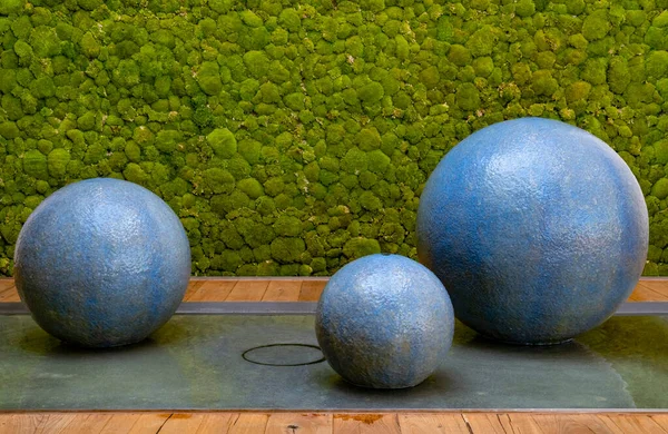 Floating sphere fountain with blue spheres in front of a green mossy wall