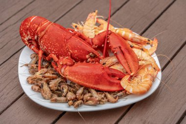 Closeup shot of a cooked lobster and some other crayfish on a plate on wooden planks clipart