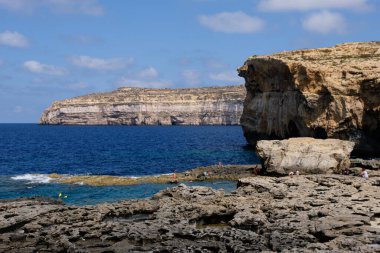 Turistler sarımsı kahverengi kireçtaşı kayalıklarının altındaki ferahlatıcı suyun tadını çıkarıyorlar - San Lawrenz, Malta