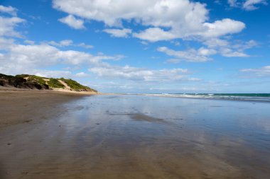 Gökyüzü ve bulutlar alçak gelgitte ıslak kuma yansıyor Torquay, Victoria, Avustralya