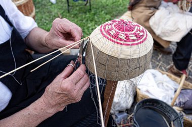 Elderly person's hands busy building a basket by weaving branches. The art of wicker weaving