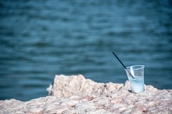 在海边的岩石上放了根稻草的塑料杯鸡尾酒 — 图库照片