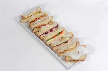 Kürdanla bir arada tutulan kulüp sandviçi, bir sürü lezzetli malzemeden ve sostan oluşur, beyaz tabakta ve arka planda.