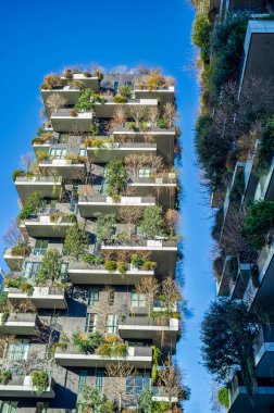 İtalya 'nın Milano bölgesindeki Porta Nuova bölgesinde bulunan ünlü ekolojik sürdürülebilir konut kompleksi Dikey Orman' ın yakın görüntüsü. Görüntü, kışın ağaçlarla ve çıplak bitkilerle kaplı balkonları ve taşrada koyu mavi bir gökyüzünü gösteriyor.