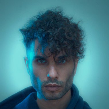 Portrait of a man with curly hair under blue lighting, exuding a mysterious and intense expression clipart