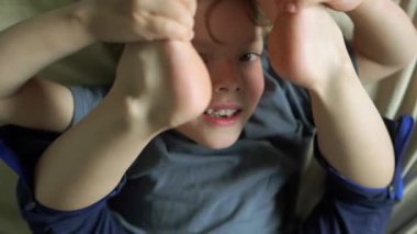 Yatakta gülümseyen 6 yaşındaki bir çocuğun yakın plan portresi. Yüksek kalite 4K görüntü. Mutlu şirin çocuk gülümseyip yatağında oynaşıyor. Yakından bir gülümseme, dişleri ve baklavaları..