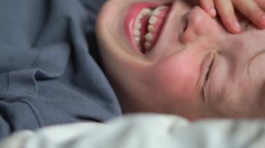 Yatakta gülümseyen 6 yaşındaki bir çocuğun yakın plan portresi. Yüksek kalite 4K görüntü. Mutlu şirin çocuk gülümseyip yatağında oynaşıyor. Yakından bir gülümseme, dişleri ve baklavaları..