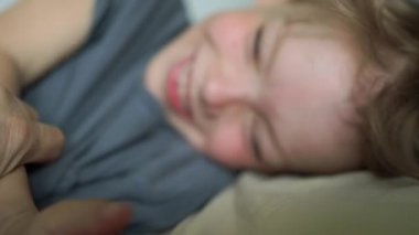 Yatakta gülümseyen 6 yaşındaki bir çocuğun yakın plan portresi. Yüksek kalite 4K görüntü. Mutlu şirin çocuk gülümseyip yatağında oynaşıyor. Yakından bir gülümseme, dişleri ve baklavaları..