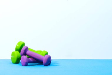 Yeşil ve mor halterlerin minimalist görüntüsü temiz beyaz arka planlı mavi egzersiz paspasına yerleştirilmiş. Fitness sadeliği, refah ve aktif yaşam temaları için mükemmel..