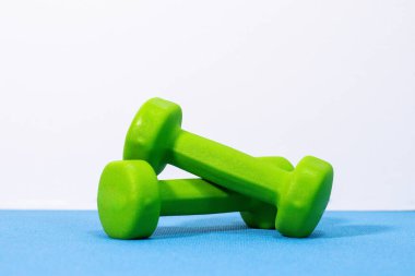 Yeşil ve mor halterlerin minimalist görüntüsü temiz beyaz arka planlı mavi egzersiz paspasına yerleştirilmiş. Fitness sadeliği, refah ve aktif yaşam temaları için mükemmel..