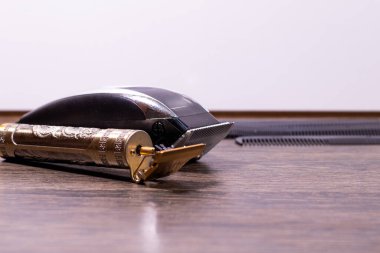 Arkaplanda taraklar olan ahşap bir yüzeyde altın ve siyah elektrikli saç kesicilerin yan görüntüsü.
