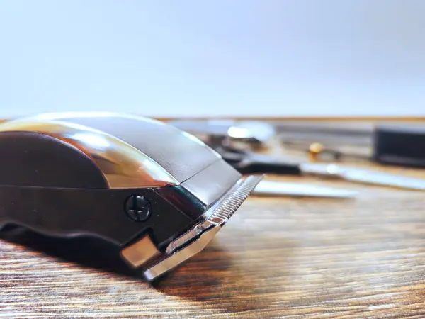 Arka planda bulanık berber aletleriyle ahşap bir masaya yerleştirilmiş elektrikli saç makasının yakın çekimi..