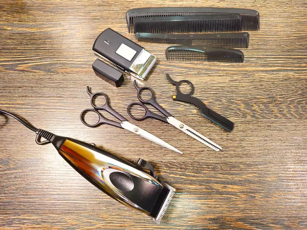 Bir elektrikli makas, kablosuz budama makinesi, çeşitli taraklar, iki çift makas ve seyreltici makas da dahil olmak üzere ahşap bir yüzeye düzgünce yerleştirilmiş profesyonel kuaför aletleri..