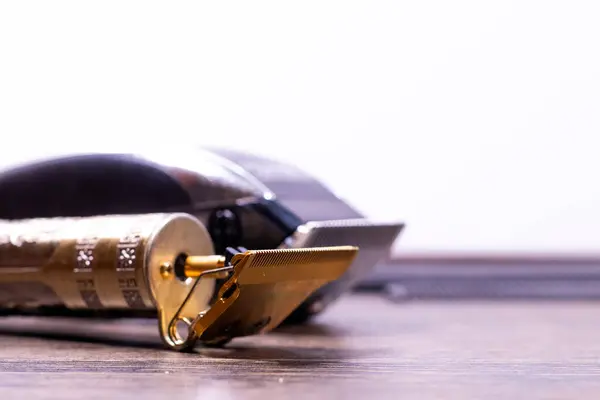 Arkaplanda taraklar olan ahşap bir yüzeyde altın ve siyah elektrikli saç kesicilerin yan görüntüsü.