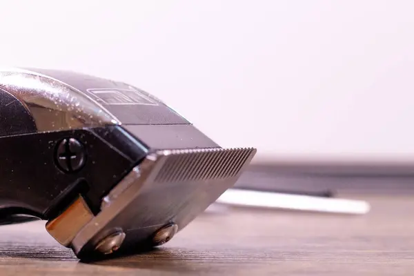 Arka planda bulanık berber aletleriyle ahşap bir masaya yerleştirilmiş elektrikli saç makasının yakın çekimi..