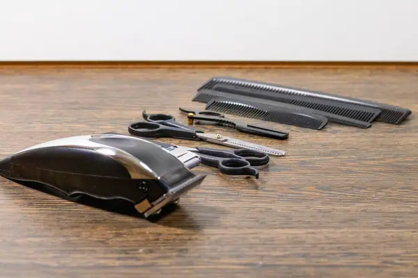 Elektrikli saç makasları, makas, tarak ve jilet de dahil olmak üzere koyu ahşap bir yüzeye yerleştirilmiş berber aletleri koleksiyonu..