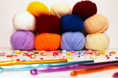 Örgü kancalı renkli iplik topları, temiz bir arkaplana karşı dizilmiş. Kırmızı, sarı, mavi, mor ve bej gibi çeşitli renkler, el işi, örgü ve örgü projeleri için idealdir..