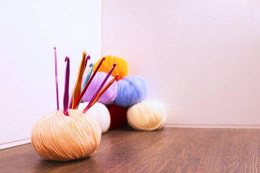 Ahşap bir yüzeye dizilmiş renkli iplik topları ve kanca koleksiyonu. İplik topları turuncu, sarı, mavi, mor, kırmızı ve beyaz gibi çeşitli tonlarda.. 
