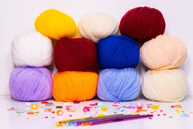 Örgü kancalı renkli iplik topları, temiz bir arkaplana karşı dizilmiş. Kırmızı, sarı, mavi, mor ve bej gibi çeşitli renkler, el işi, örgü ve örgü projeleri için idealdir..