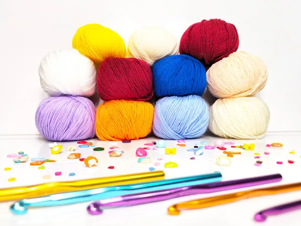 Örgü kancalı renkli iplik topları, temiz bir arkaplana karşı dizilmiş. Kırmızı, sarı, mavi, mor ve bej gibi çeşitli renkler, el işi, örgü ve örgü projeleri için idealdir..