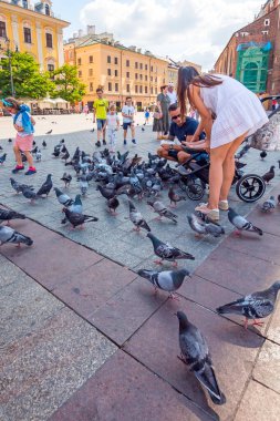 Cracow, Poland: 23 July 2022: People feed pigeons, tourists attraction in Main Market Square in the Old city of Cracow, Poland.