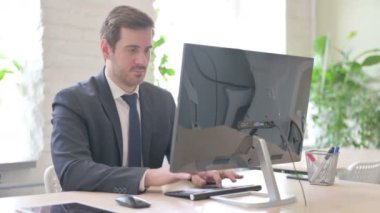 Genç Yetişkin İşadamı Masaüstü Bilgisayarını Kullanırken Kameraya Gülümsüyor