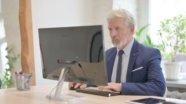 Alter Geschäftsmann Blickt Auf Kamera Während Desktop Computer Benutzt — Stockvideo