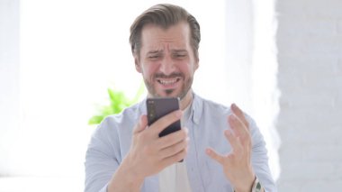 Mature Man Reacting to Loss on Smartphone
