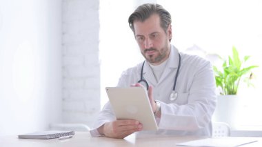 Male Doctor using Tablet while Sitting in Clinic