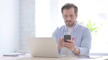 Mature Man using Smartphone while using Laptop