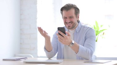 Upset Mature Man Reacting to Loss on Smartphone in Office