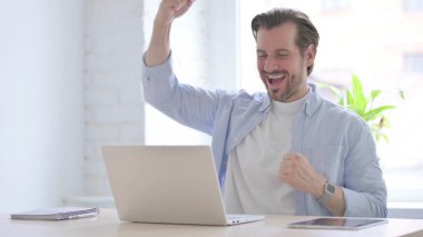 Mature Man Celebrating Online Success in Office