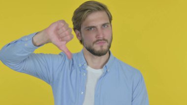 Thumbs Down by Casual Young Man on Yellow Background