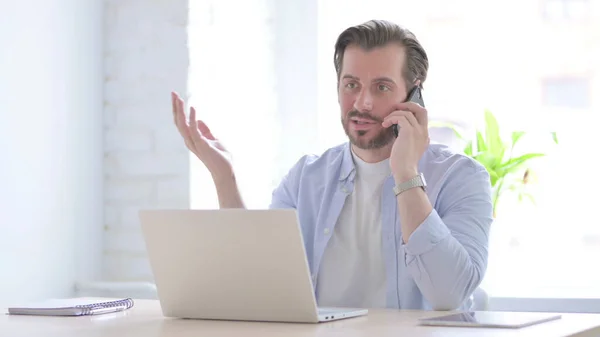 Mature Man Talking Phone While Using Laptop — Stockfoto