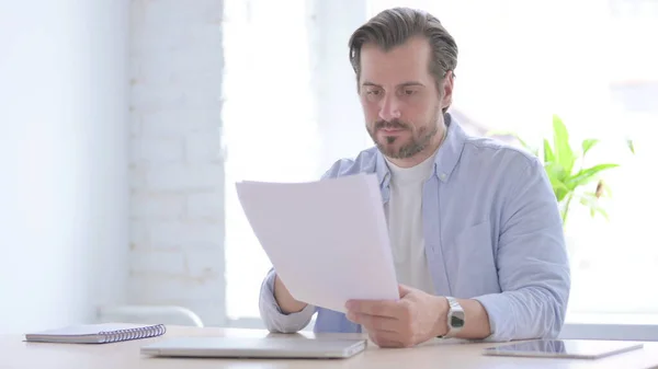 Mature Man Reading Reports While Sitting Office — Stockfoto