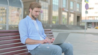 Orta yaşlı adam bankta dizüstü bilgisayar kullanmakla meşgul.