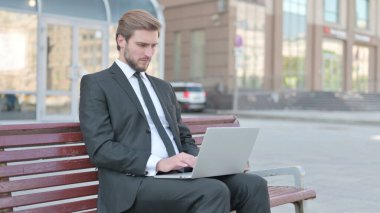 Busy Middle Aged Businessman Using Laptop Sitting Outdoor on Bench